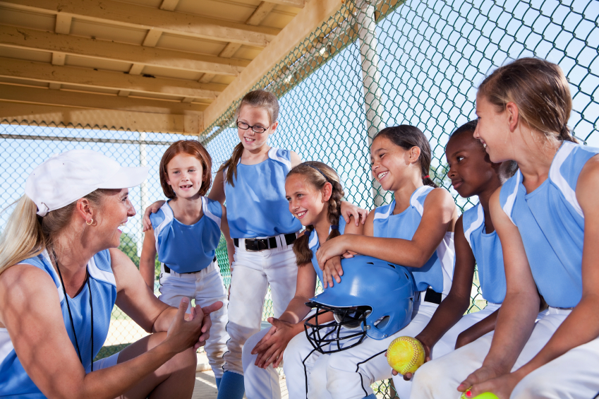Softball team:  Coach (40s) with girls (7-10 years) in dugout.